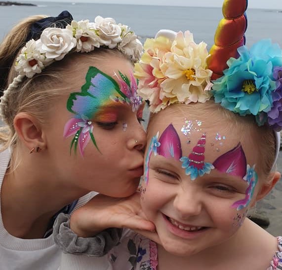 Young girl with face paint kissing toddler's cheek.
